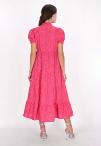 Rochie midi roz cu mâneci umflate, design în straturi și model floral. Prezintă o croială lejeră și un margine evazată. Sandale argintii cu barete vizibile.