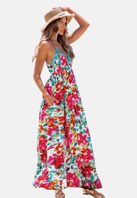 Robe maxi blanche avec un imprimé floral vibrant en rose, orange et teal. Présente une taille froncée et des poches. Accessoirisée avec un chapeau en paille.