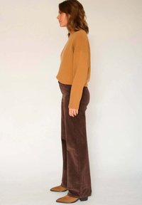 Pantalons larges en velours côtelé marron associés à un pull en tricot beige. Texture lisse, coupe décontractée et manches de chemise retroussées. Chaussures pointues marron.