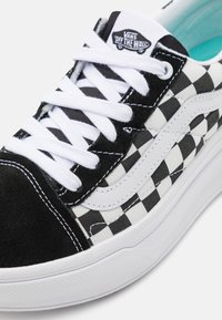 Baskets en toile à carreaux noir et blanc avec des accents en daim noir, des lacets blancs et une semelle blanche. Présente le logo Vans sur la languette.