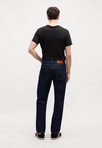 Temno modre jeans hlače s ravnim krojem, rjava usnjena etiketa na pasu in dve zadnji žepki. Nosi se z belo majico.