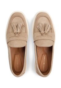 Μπεζ μοκασίνια από σουέτ με διακοσμητικές φούντες, στρογγυλεμένη μύτη και λευκή σόλα από καουτσούκ. Καφέ εσωτερικό με οπές για καλύτερο αερισμό.
