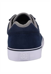 Navy blue suede skate shoe with a grey fabric collar, white rubber sole, and rear DC logo. Smooth surface with a slight sheen.