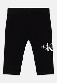 Svarta leggings tillverkade av mjukt material, med en vit "CK" logotyp och text på nedre sidan. Midje med hög mittpunkt och elastiskt band.