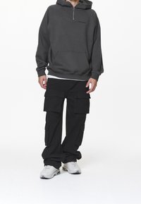 Grå zip-up hoodie med framficka, kombinerad med svarta cargobyxor med flera fickor. Skor är grå sneakers.