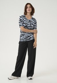 Črno-bela majica kratkih rokavov s potiskom zebra, kombinirana z ohlapnimi črnimi hlačami in belimi supergami. Preprost, priložnostni dizajn.