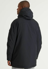 Crna kapuljača s glatkom teksturom, zatvaranjem na patentni zatvarač i podesivom kapuljačom. Stražnji dio prikazuje detalje šavova na ramenima i opušteni kroj.