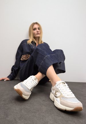 Zapatillas blancas con acentos en gris y beige, malla texturizada y suela de goma. Presentan un logo en el lado y cordones planos.