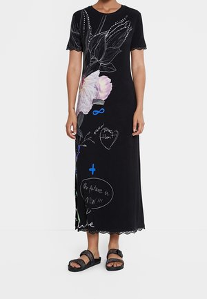 Czarna maxi sukienka w kwiatowy wzór, z napisami i koronkową lamówką na rękawach. Noszona z czarnymi sandałami z regulowanymi paskami.