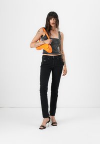Black high-waisted jeans with a slim fit, paired with a black and white polka dot crop top. The outfit features a bright orange handbag and black heels.
