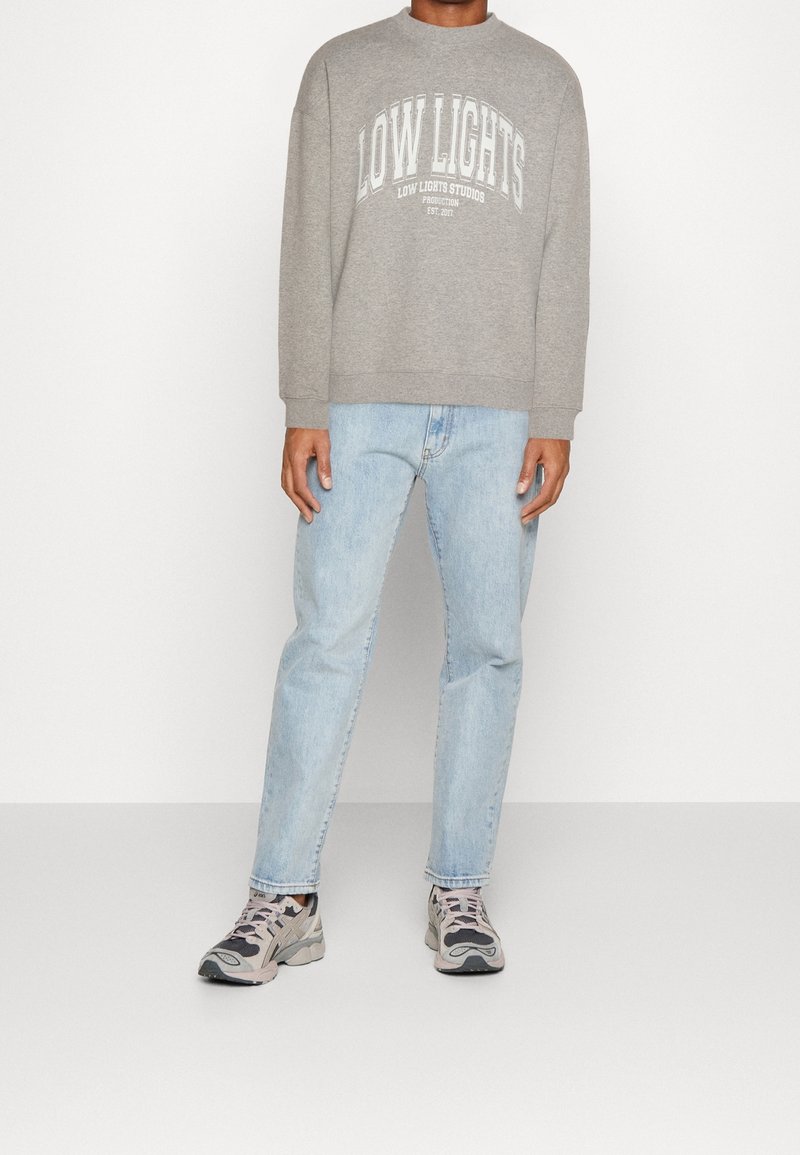 Sudadera gris con gráfico de "LOW LIGHTS", combinada con jeans de mezclilla azul claro y zapatillas deportivas multicolores. Diseño y ajuste casual.