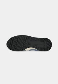 Black rubber shoe sole with aggressive tread pattern and raised accents, featuring a section in cream. Textured surface for grip.