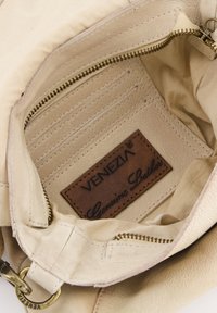 Innenteil einertan ledernen Handtasche mit beigem Futter, mehreren Kartenfächern und einer Reißverschlusstasche. Mit einem "VENEZIA Echtes Leder"-Etikett.