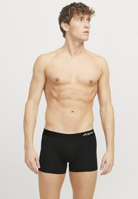 Black boxer shorts with a wide elastic waistband featuring a logo, constructed from a smooth fabric, fitted design, mid-thigh length.