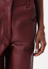 Bordeauxleren broek met een soepele textuur, voorzien van zijzakken en een getailleerde pasvorm. Zichtbare stiksels en een strakke vorm accentueren de stijl.