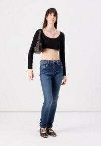 Black cropped long-sleeve top, blue skinny jeans, and animal print flats. Gray bag with strap. Model stands against a plain background.
