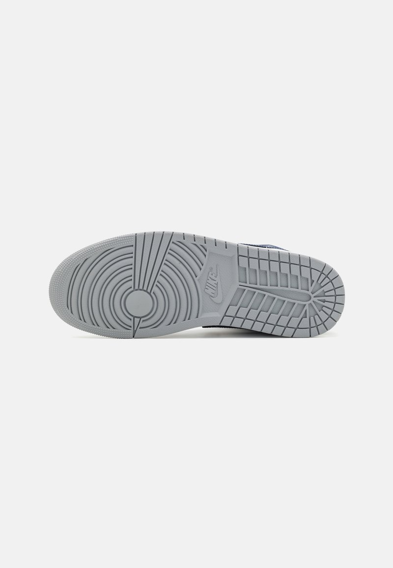 Suela de goma gris de una zapatilla Nike que muestra patrones de tracción circulares y de rejilla, con el logo de Nike grabado cerca del arco.