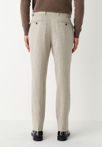 Pantalon gris clair sur mesure en tissu texturé, avec deux poches arrière à boutons et une coupe droite.