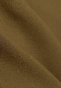 Gros plan d'un tissu doux et texturé de couleur olive-brun unie avec des plis légers créant des ombres et des reflets.