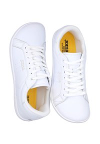 Zapatillas blancas fabricadas con material sintético suave, con un diseño limpio, punta redonda y cordones. Planta amarilla con el nombre de la marca "Joma".