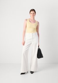 Yellow ribbed tank top, white wide-leg pants, black pointed heels, and a textured black handbag, set against a plain white background.