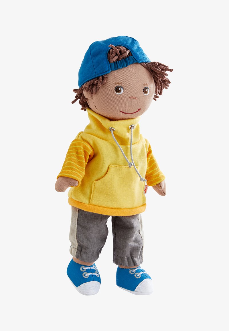 Weiche Puppe mit braunem Garnhaar, die eine umgedrehte blaue Mütze, einen gelben Kapuzenpullover mit gestreiften Ärmeln, graue Hosen und blaue Turnschuhe trägt.