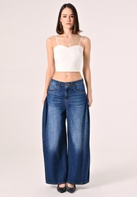 Top bianco corto con spalline sottili, abbinato a jeans a gamba larga in denim scuro. I jeans hanno un design a cinque tasche e una chiusura con bottone classica.