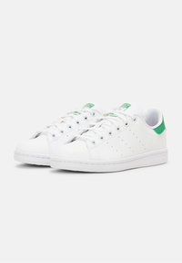 Bílé tenisky Adidas Stan Smith s zeleným podpatkem a logem na jazyku, bílé šnůrky a perforované postranní pruhy, zobrazené z přední bočního úhlu.