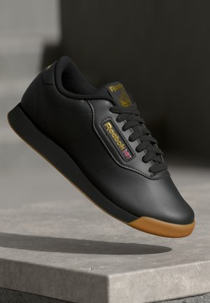 Black leather sneaker with yellow accents and logo, featuring a textured surface, laces, and a gum sole. Lightweight with a streamlined design.