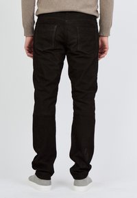 Mustat mokkahousut, joissa on slim fit -leikkaus, pehmeä pinta ja kaksi takataskua, yhdistettynä harmaisiin tennareihin ja vaaleanbeigeen neuleeseen.