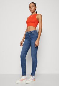 Red cropped tank top paired with blue skinny jeans, showcasing a smooth denim texture. White sneakers with light purple accents complete the outfit.