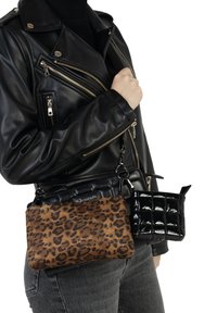 Persona che indossa una giacca di pelle nera e jeans grigi con tre borse a tracolla: una a stampa leopardata, una nera imbottita e una nera in ecopelle.