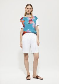 Bluse mit Blumenmuster in Teal, weiße Kurzarm; weiße plissierte Shorts; braune flache Sandalen; minimalistisches Design, glatte Textur.