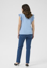 Top azzurro chiaro a maniche corte con spalle arricciate, abbinato a jeans dritti blu scuro e scarpe con tacco nere. Vista posteriore.