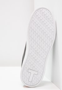 Podešev boty se vzorovanou texturovanou bílou gumovou základnou a hladkým šedým horním dílem. Tvarové logo vyražené na podešvi.