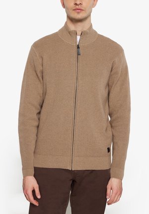 Brun zip-up sweater med et struktureret strikmønster, høj krave og ribbede manchetter. Sort logoaccent på den nederste venstre side.