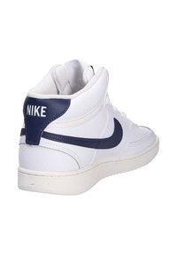 Sneaker alta in pelle bianca con accenti blu navy, dotata di collo imbottito e suola testurizzata, logo in evidenza sul tallone.