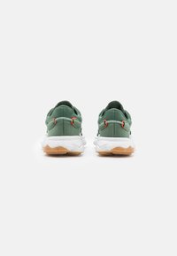 Green fabric sneakers with white soles, featuring orange accents and a textured back heel. Rounded design with padded collar.