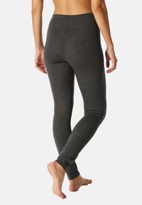 Grijze, nauwsluitende legging met een gladde textuur, hoge tailleband en taps toelopende enkels. Het materiaal lijkt rekbaar voor comfort en gemakkelijke beweging.
