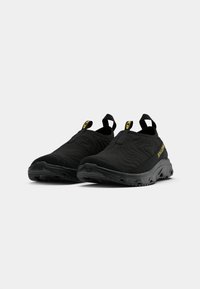 Black slip-on shoes with a textured fabric upper, featuring a molded rubber sole and yellow logo accents on the side and heel.