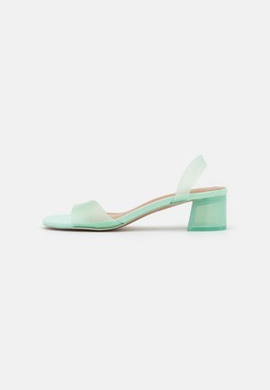 Sandale slingback vert menthe, à bout ouvert, avec une finition lisse, dotée d'une bride large et d'un talon bloc transparent pour un soutien supplémentaire.