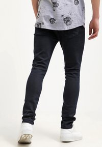 Dark skinny jeans with a smooth texture, featuring a classic five-pocket design. Paired with white sneakers and a gray floral T-shirt.