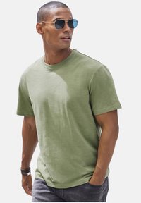 Olive green cotton t-shirt with a crew neck and short sleeves, paired with silver-framed sunglasses. Smooth texture and simple design.