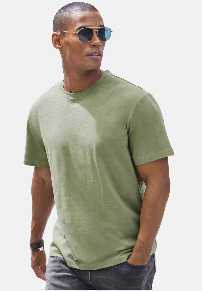 Olive green cotton t-shirt with a crew neck and short sleeves, paired with silver-framed sunglasses. Smooth texture and simple design.