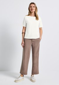 T-shirt bianco in cotone con maniche corte abbinato a pantaloni larghi beige in felpa con strisce laterali e texture liscia, indossato con sneaker.