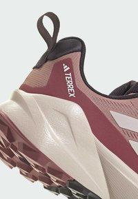 Scarpa da trekking Terrex in bordeaux e grigio, con upper testurizzato, resistente intersuola bianca e suola nera robusta con tasselli per la trazione.