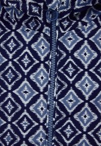 Mörkblå zip-up-plagg med ett diamantmönster i ljusblå nyanser, med slät yta och en central dragkedja.