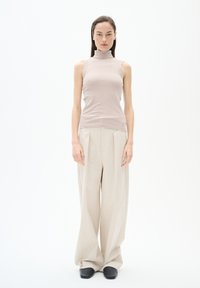 Top senza maniche a collo alto beige a coste dal design aderente, abbinato a pantaloni beige a vita alta e gamba larga, insieme a scarpe slip-on nere.