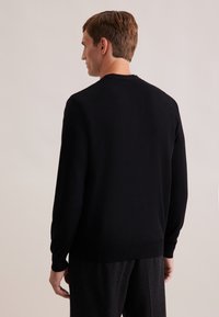 Pull noir en tricot avec des manches longues et un col rond. Texture douce, poignets et ourlet ajustés, montrant une silhouette légèrement cintrée.