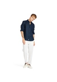 Camisa de lino azul marino de botones con mangas largas, combinada con pantalones de lino blancos y zapatillas de color claro. Diseño simple, sin patrones visibles.